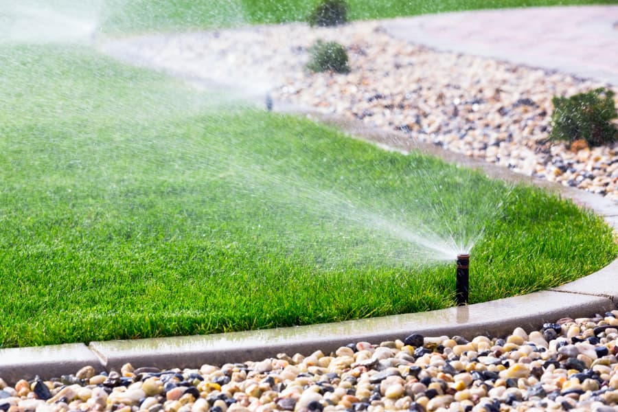 Irrigation system applying water to green grass next to stone pathway