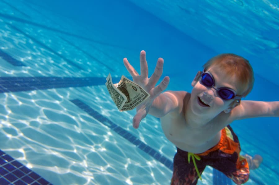 Young swimmer underwater reaching for dollar bill